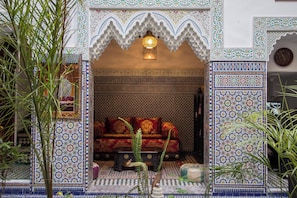 An ornate entrance with intricate tile work, a seating area with patterned cushions, and a hanging light fixture. - Ryad Naila  (Fès)