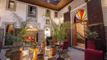 A traditional Moroccan interior with ornate tile work, a central fountain, and a seating area with a red sofa.