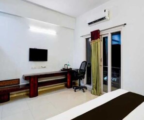 Une chambre d’hôtel comprenant un lit, un bureau avec une chaise, un téléviseur à écran plat et une fenêtre avec des rideaux.