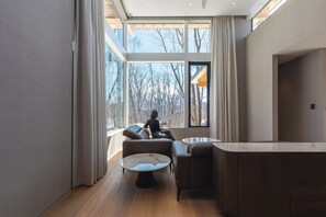 A modern living room with a large window, a sofa, a coffee table, and a wooden cabinet.