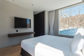 A modern bedroom with a large bed, a mounted TV, and a window with a view of trees. - Yuki Drift (Kutchan-cho, Abuta-gun)