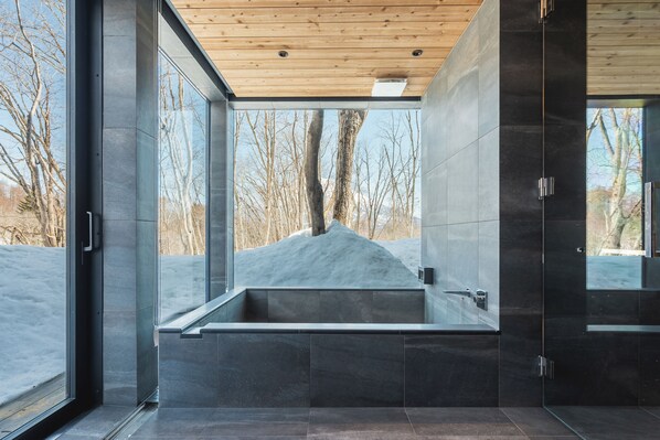 A modern bathroom with a large bathtub, glass walls, and a view of a snowy landscape.
