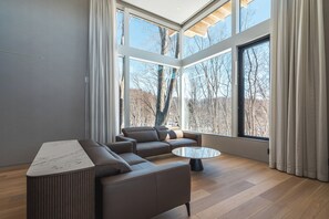 A modern living room with a sectional sofa, a coffee table, and large windows offering a view of trees.