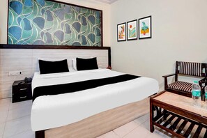 Ein Hotelzimmer mit Bett, Nachttisch, Stuhl und einem Kunstwerk an der Wand.