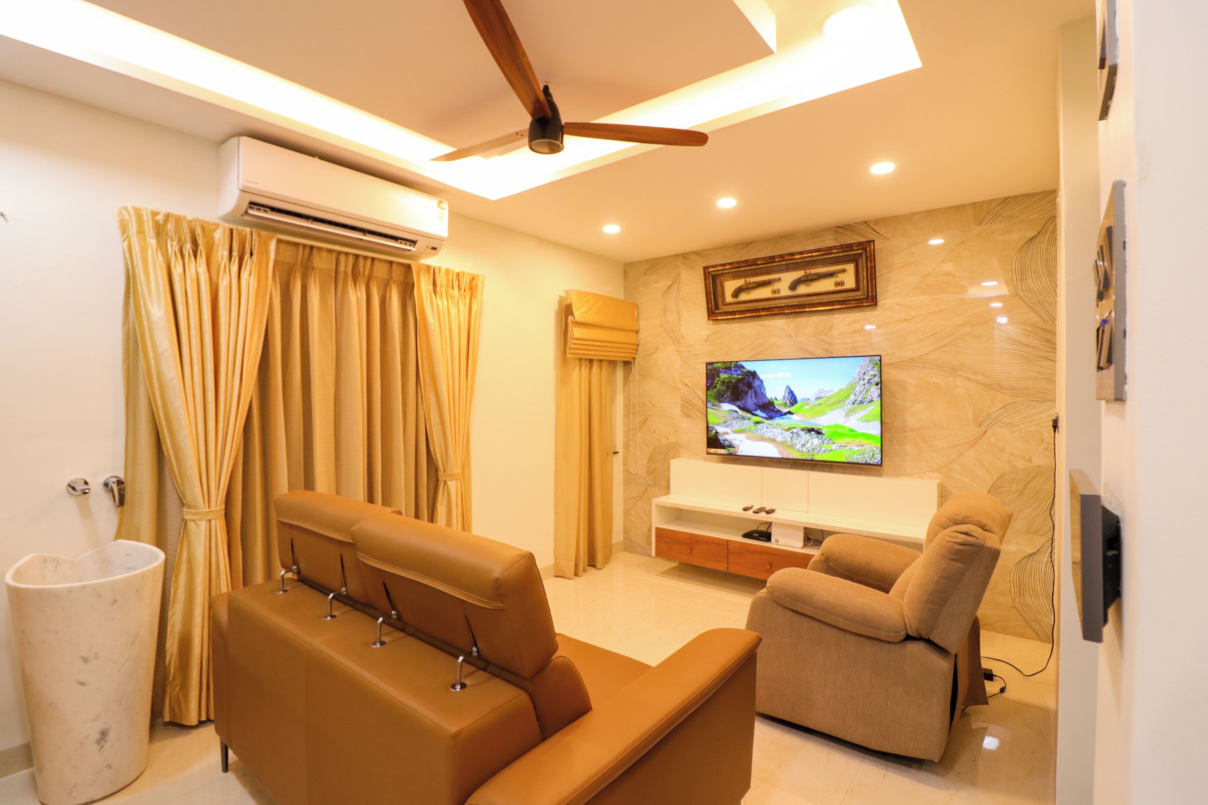 A modern living room with a sofa, a recliner, a TV mounted on the wall, and an air conditioning unit.