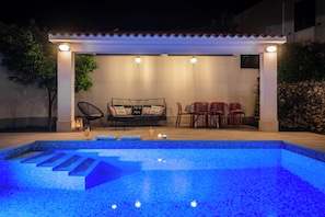 Un espace piscine extérieur doté d’un coin salon abrité, d’un canapé et d’une table avec des chaises.