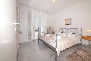 Une chambre à coucher avec un lit, une table de chevet, une lampe, un tableau et une vue sur l’extérieur, visible à travers une porte.
