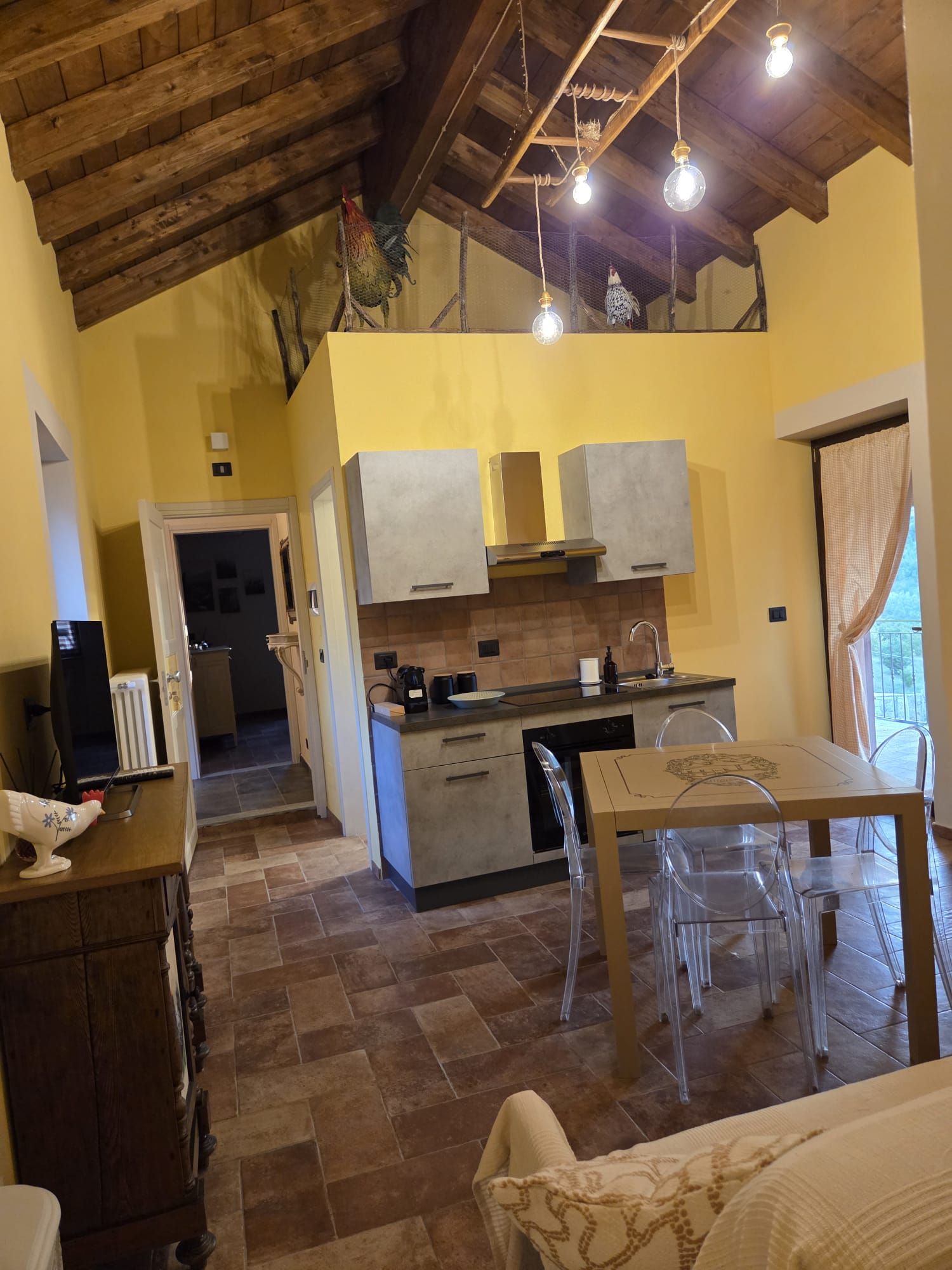A compact kitchen with a dining area, wooden ceiling beams, and a view through a window.