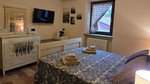 A bedroom with a bed, dresser, television, window with curtains, and a radiator. - LA NOCCIOLINA CASCINA MOSE, nestled in nature among farm animals (Ovada)