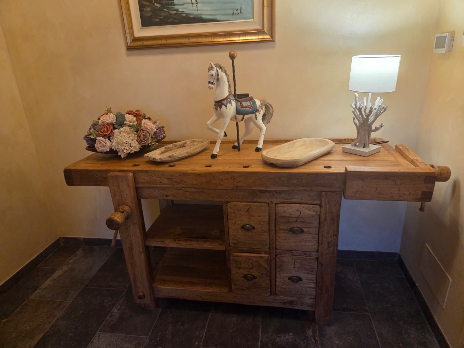 Una scrivania in legno con una statuina di cavallo decorativa, una lampada e un bouquet di fiori.
