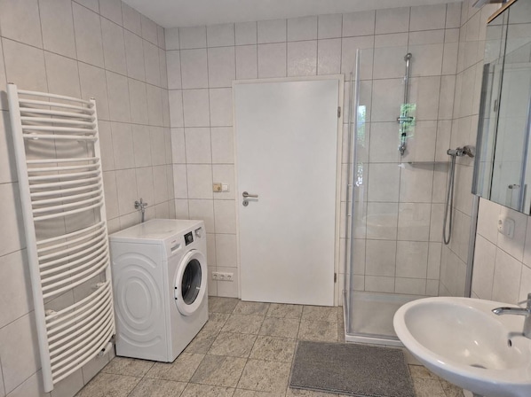 Ein Badezimmer mit Waschmaschine, Duschkabine aus Glas und Waschbecken.