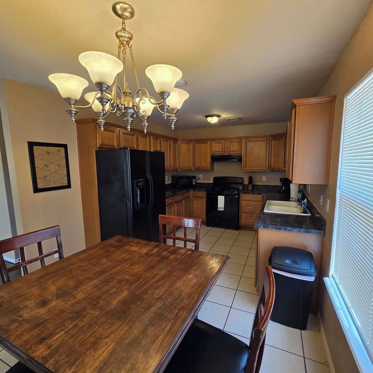 A kitchen with wooden cabinets, a black refrigerator, a stove, and a dining table with chairs.