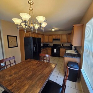 Una cocina con armarios de madera, un refrigerador negro, una estufa y una mesa de comedor con sillas.