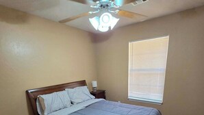 Ein Schlafzimmer mit einem Bett, einem Nachttisch, einem Deckenventilator und einem Fenster mit Jalousien.
