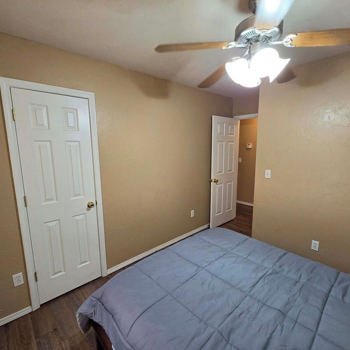 A bedroom with a bed, a ceiling fan, and a door leading to another room.
