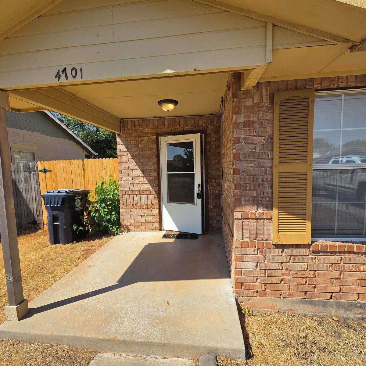 A residential entrance with a concrete porch, a brick wall, a wooden fence, and a door with a window above it.