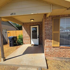 A residential entrance with a concrete porch, a brick wall, a wooden fence, and a door with a window above it.
