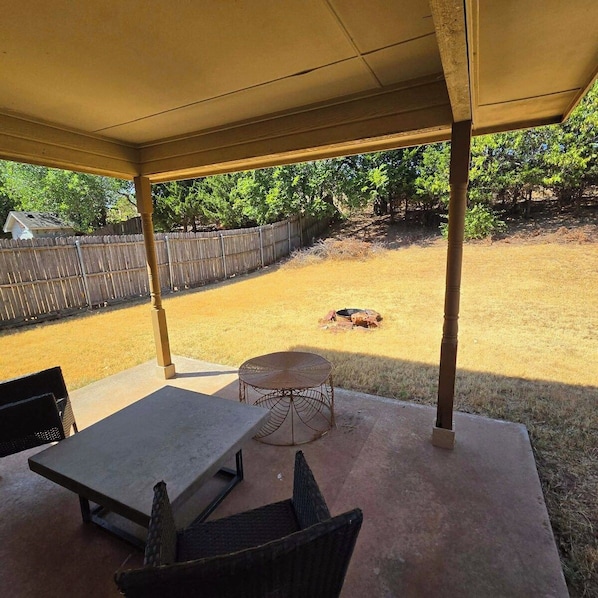 A covered patio area with a table and chairs, a fire pit, and a fenced yard.