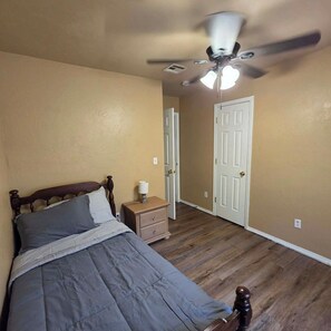 Un dormitorio con cama, mesita de noche, lámpara, ventilador de techo y una puerta.