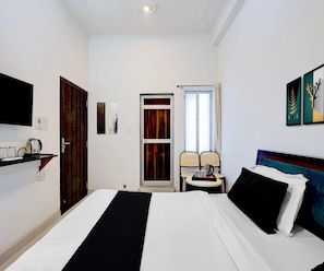 Ein Hotelzimmer mit einem Bett, einem Fernseher, einem kleinen Tisch mit Lampe und einem Fenster mit Vorhängen.