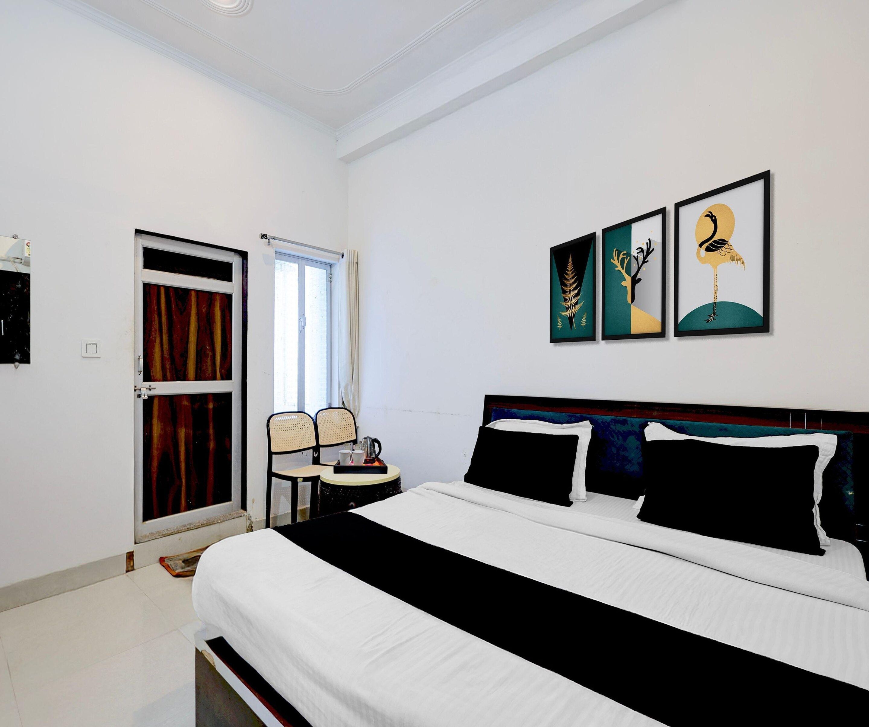 A hotel room with a bed, a chair, a table, and three framed artworks on the wall.