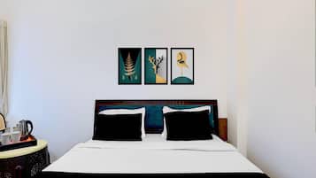Ein Hotelzimmer mit einem Bett, zwei Kissen, einem Nachttisch mit Wasserkocher und drei gerahmten Kunstwerken an der Wand.