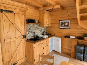 A wooden cabin interior with a kitchen area, including a stove, sink, and cabinets.