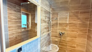 Ein modernes Badezimmer mit einer gläsernen Dusche, einem weißen Waschbecken mit zwei Seifenspendern und einem Spiegel mit Holzrahmen.