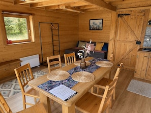 Interior de madera con una mesa de comedor, sillas, un sofá y una ventana con vista a follaje.