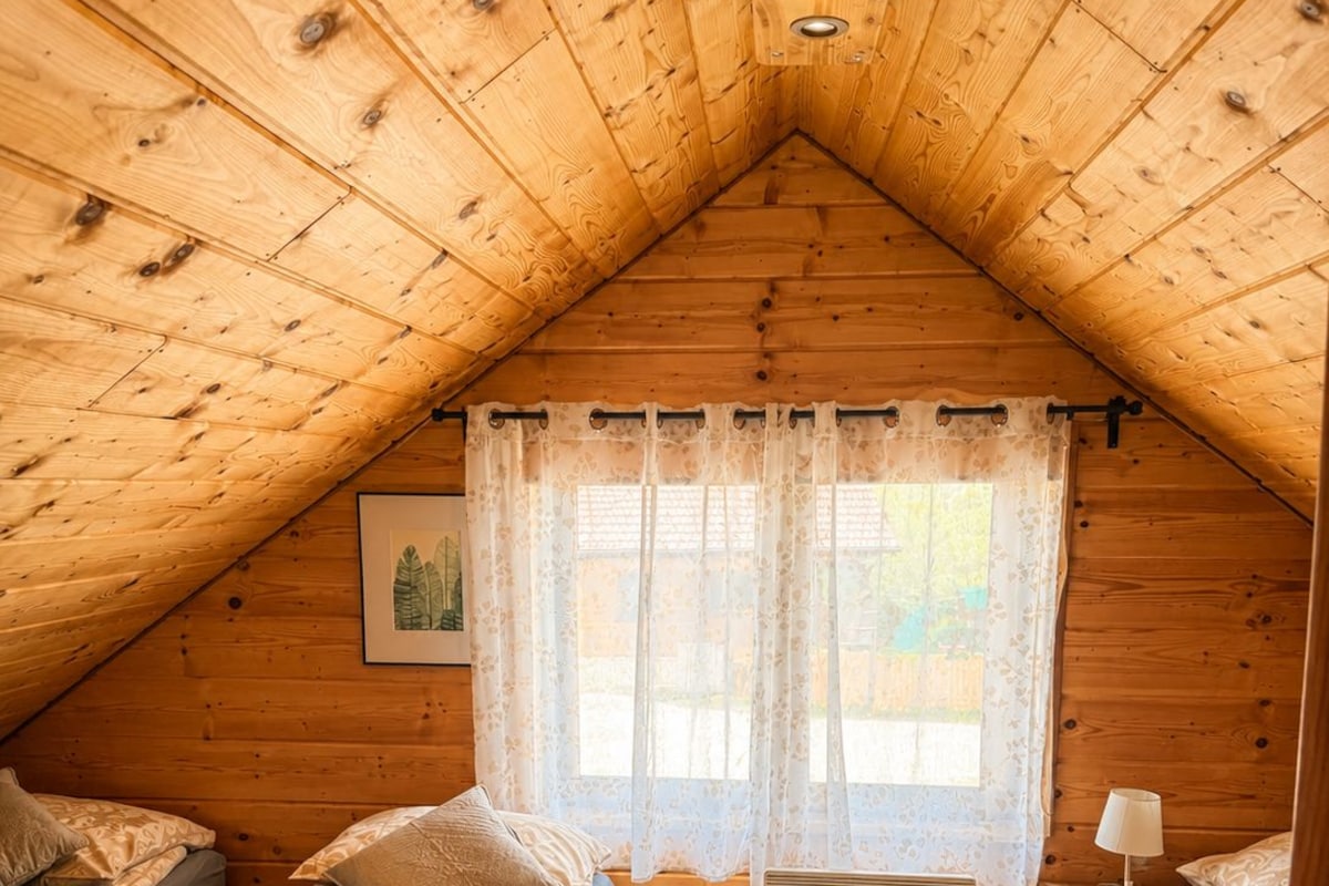 Een knus slaapkamer op zolder met twee bedden, een raam met gordijnen, een radiator en een nachtkastje met een lamp.