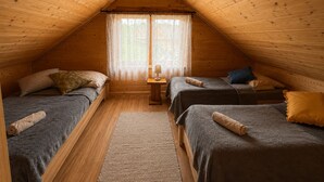 Ein gemütliches Schlafzimmer im Dachgeschoss mit zwei Betten, einem kleinen Tisch und einem Fenster mit Vorhängen.