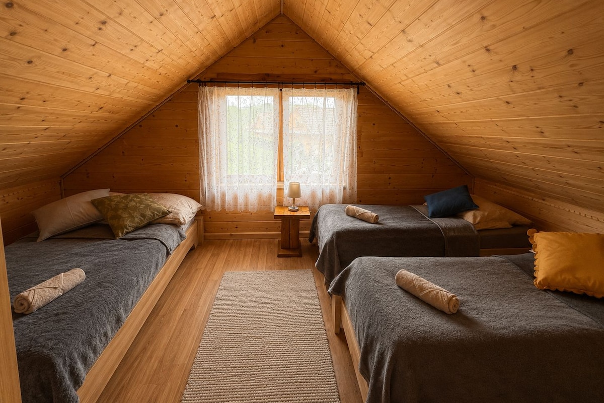 Ein gemütliches Schlafzimmer im Dachgeschoss mit zwei Betten, einem kleinen Tisch und einem Fenster mit Vorhängen.