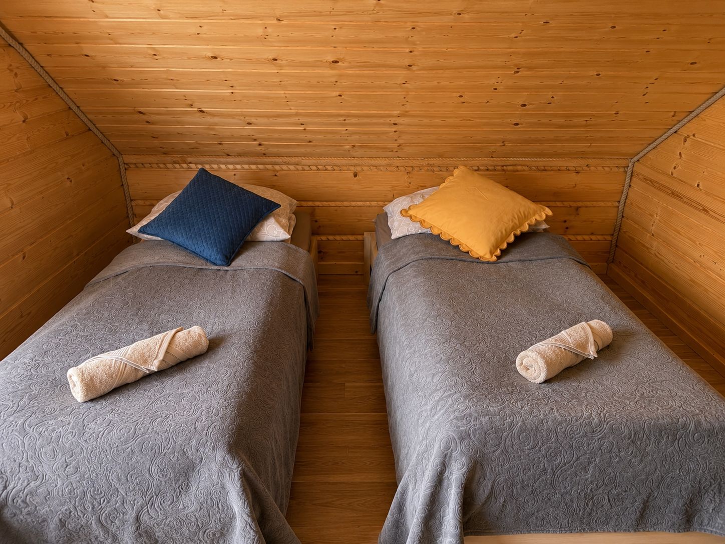 Una cabaña con dos camas individuales, cada una con una almohada y una toalla enrollada.