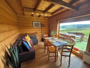 A wooden interior with a sofa, dining table, chairs, and a view through a window.