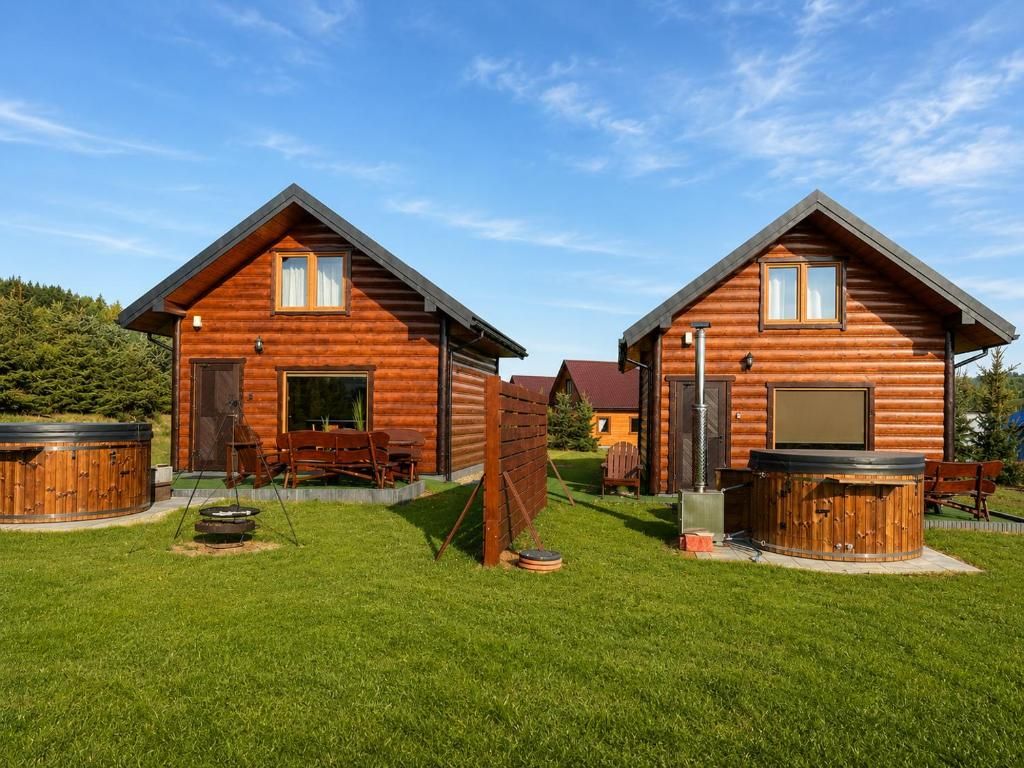 Twee houten hutten met bubbelbaden, een houten terras en een gazon.
