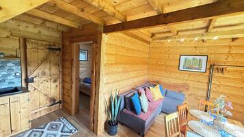 Interior de una cabaña de madera con sofá, mesa de comedor y zona de cocina.