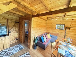Interior de una cabaña de madera con sofá, mesa de comedor y zona de cocina.