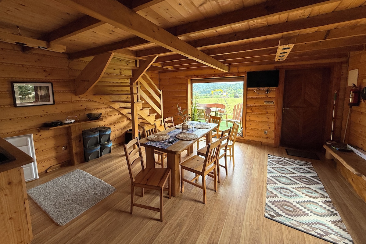 Un interior de madera con una mesa de comedor, sillas, una escalera y vistas al exterior.