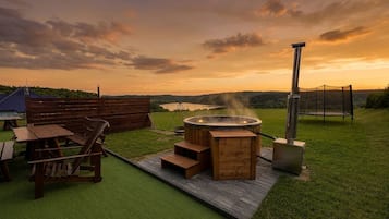 Un jacuzzi con cubierta de madera, una silla de madera y una mesa sobre un césped.