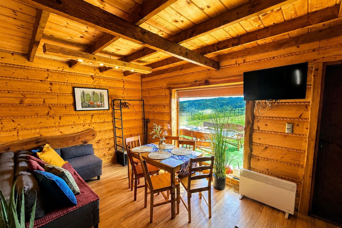 Interior acogedor de una cabaña de madera con comedor, sofá y televisor en la pared.