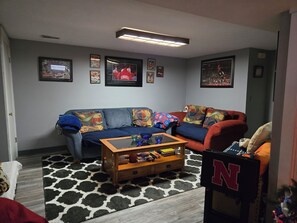 Ein Wohnzimmer mit einer Couch, einem Couchtisch und einem Teppich. An der Wand hängen gerahmte Bilder.