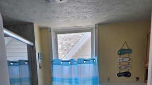 Un bagno con doccia, WC e una finestra con tenda a tema spiaggia.