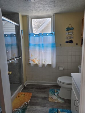 Ein Badezimmer mit Dusche, Toilette und einem Fenster mit Strandmotiv.