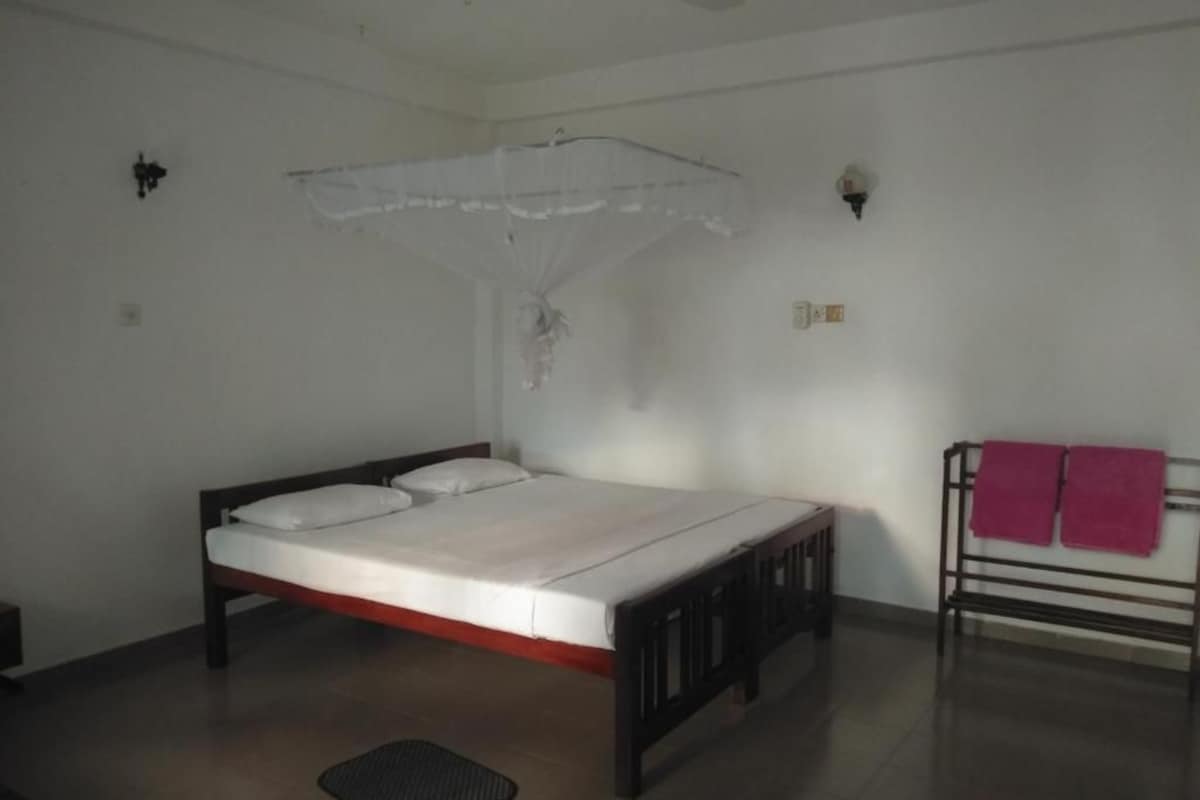 A single bed with a wooden frame and white bedding, a small bedside table, a wall-mounted light fixture, and a ceiling fan.