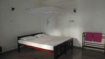 A single bed with a wooden frame and white bedding, a small bedside table, a wall-mounted light fixture, and a ceiling fan.
