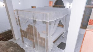 A room with a bed covered in a sheer white canopy, a wooden headboard, and a stone wall. - Rock House (Unawatuna)