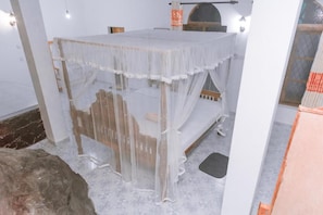 Una habitación con una cama cubierta por un dosel blanco translúcido, un cabecero de madera y una pared de piedra.