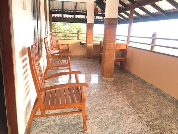 A covered outdoor seating area with wooden chairs and a tiled floor. - Rock House (Unawatuna)