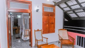 A room with a wooden door, two wicker chairs, a small table, and a ceiling fan.