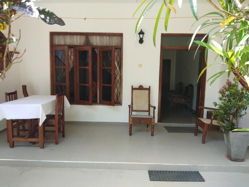 Un área de comedor al aire libre con una mesa y sillas, una silla de madera, una planta en maceta y un acceso a un espacio interior.